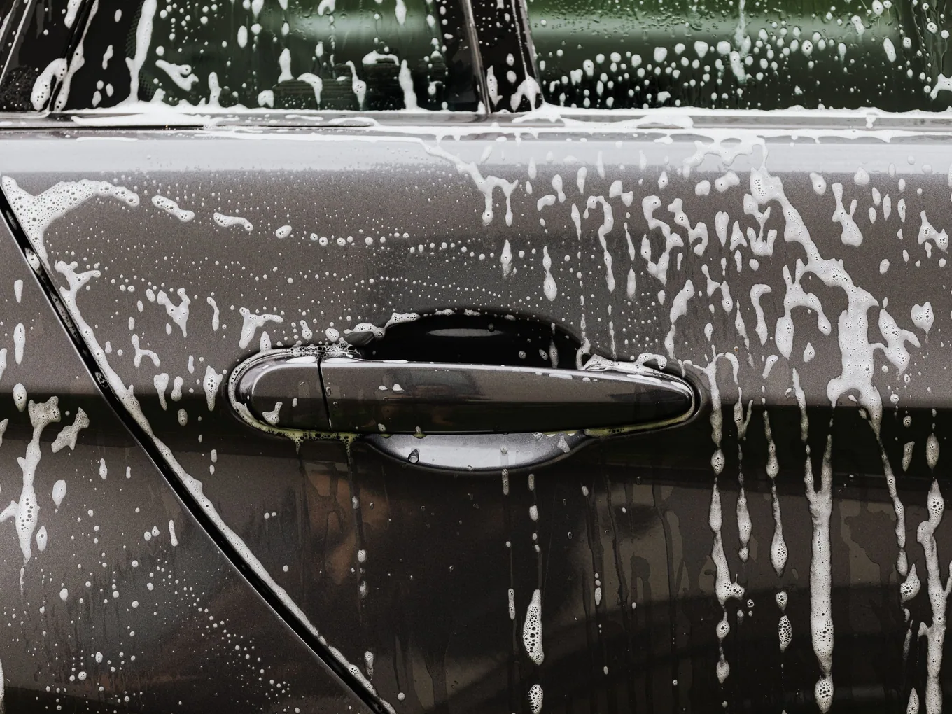 Soap suds worked across a black car door during a hand wash